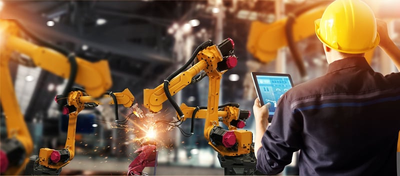 Ein Werksarbeiter hält ein Tablet in einer modernen Fabrik mit Robotern
