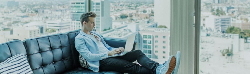 Ein Business Man sitzt in einem verglasten Büro mit hochgelegten Beinen und einem Laptop auf dem Schoß
