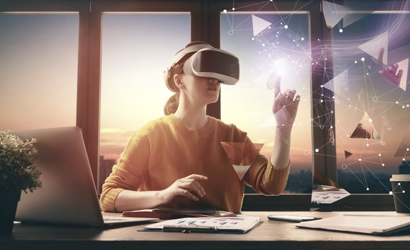 Eine Frau sitzt am Schreibtisch und hat eine AR/VR-Brille auf