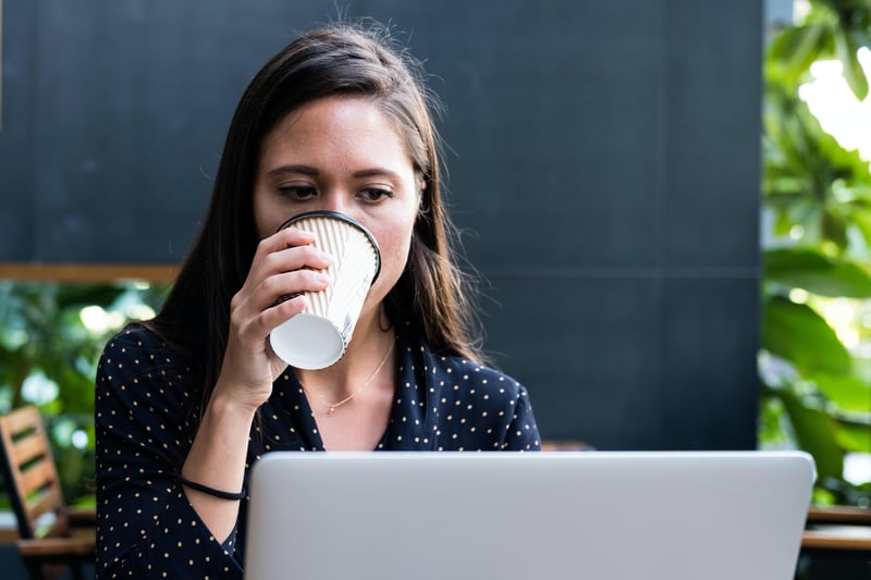 Frau trinkt Coffee-2-Go vor dem Laptop